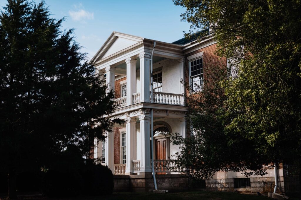 A stately two-story brick house with white columns and a balcony, surrounded by lush greenery in Williamson County, Tennessee.