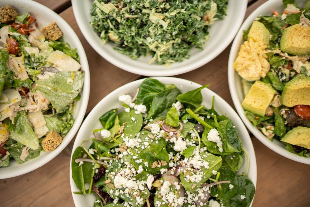 Four bowls of colorful salads with various toppings on a wooden table in Williamson County, Tennessee.