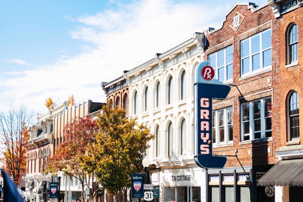 A row of colorful autumn trees lines a street with historic brick buildings and vintage signs in Williamson County, Tennessee.