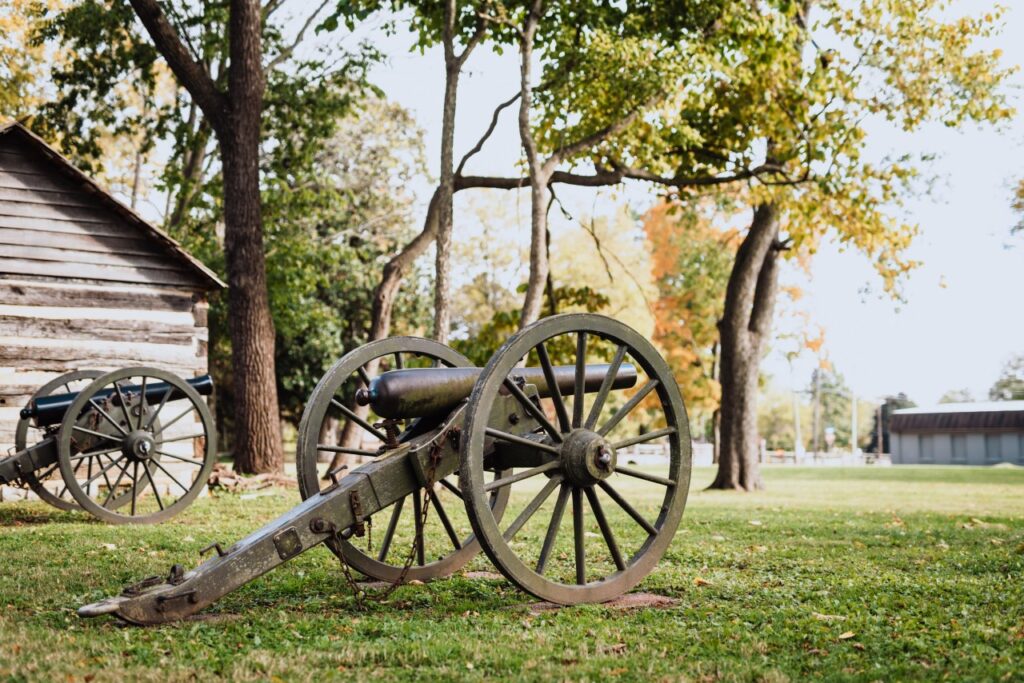 Two antique cannons with wooden wheels rest on a grassy field near a log cabin in Williamson County, Tennessee.