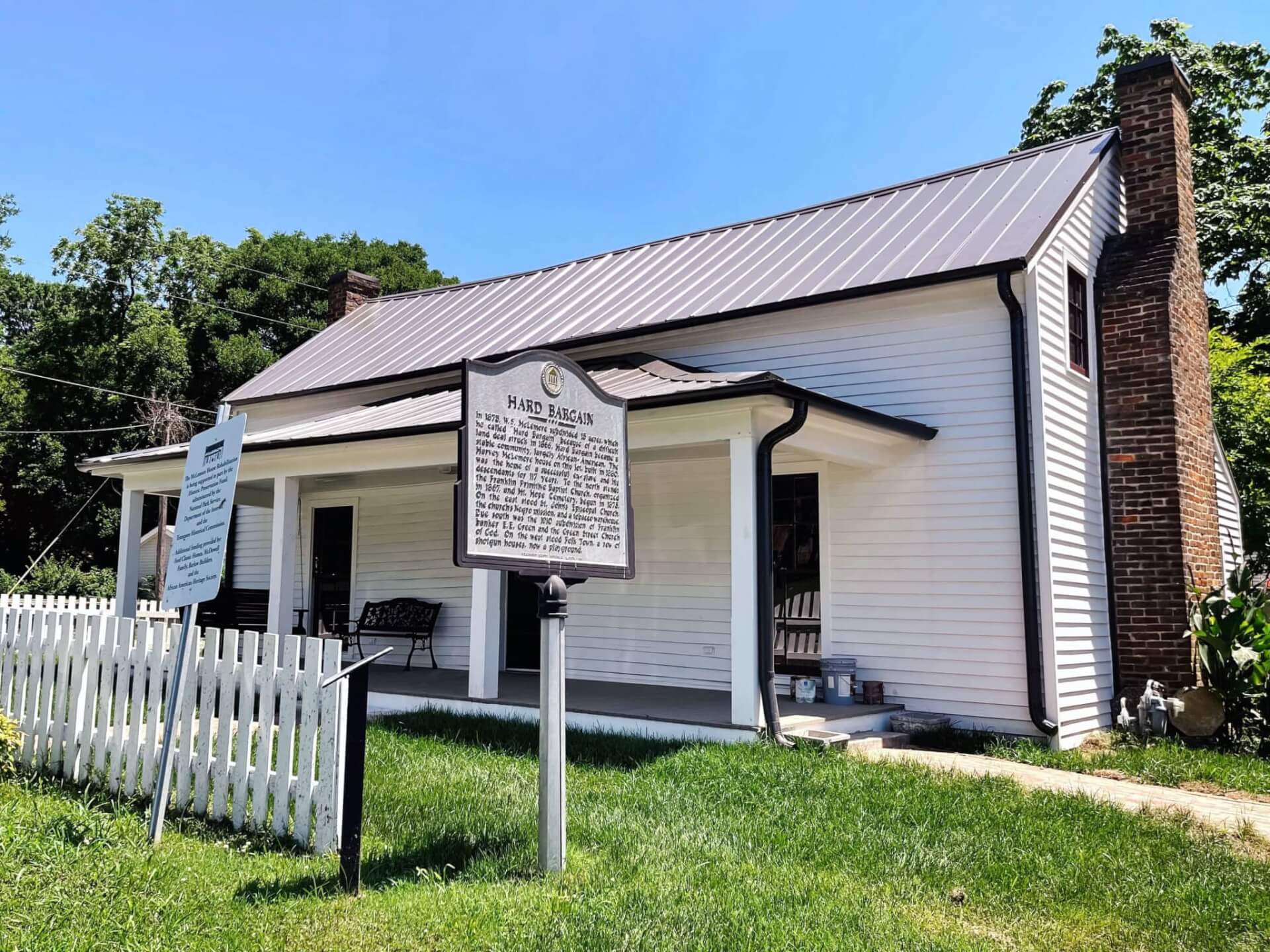 White house with metal roof, brick chimney, and porch, surrounded by green lawn and white picket fence in Williamson County, Tennessee.