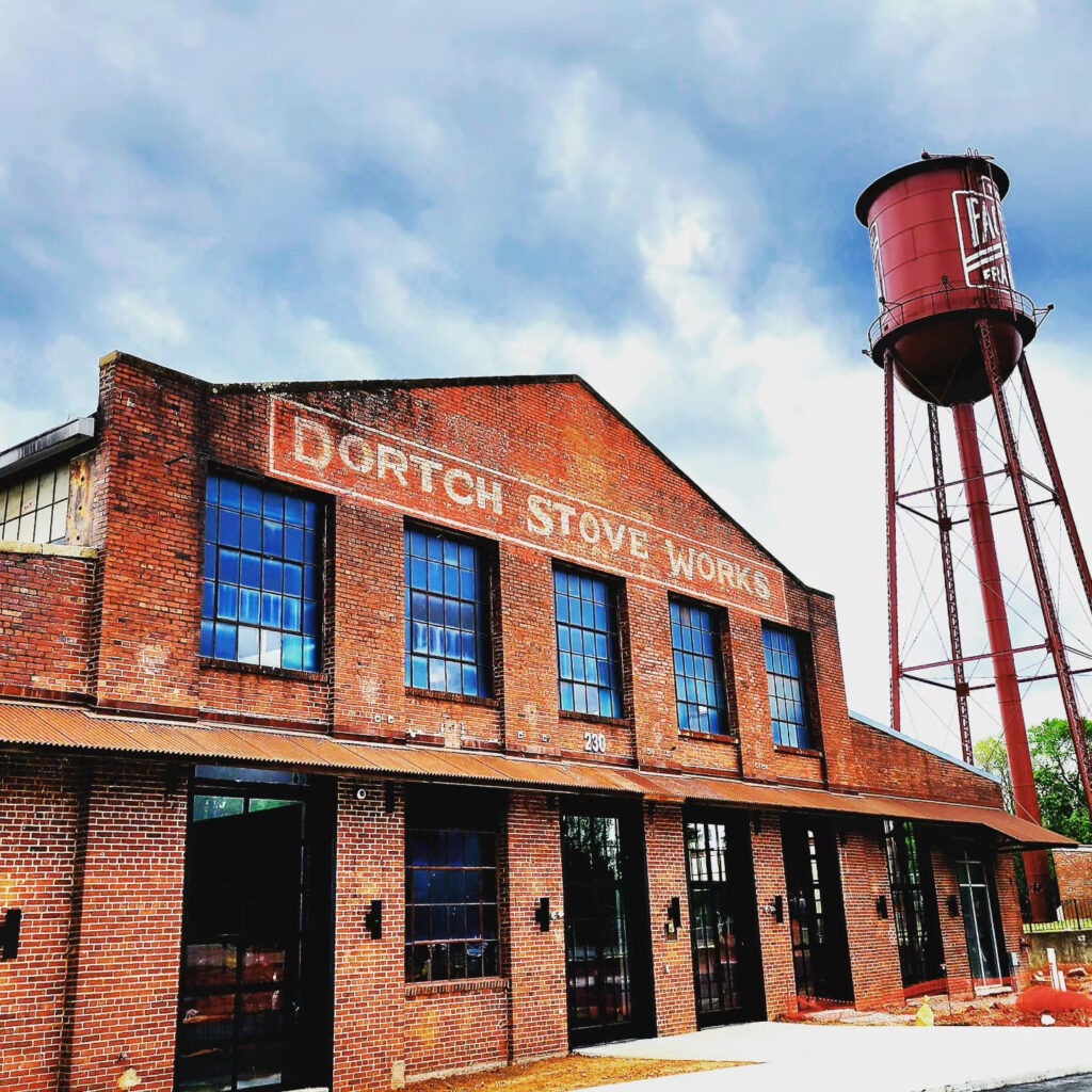 A historic brick building with large windows and a sign reading 'Dortch Stove Works' stands next to a red water tower in Williamson County, Tennessee.