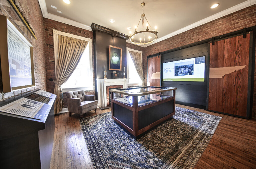 A historic room with a fireplace, wooden floor, and a central display table in Williamson County, Tennessee.