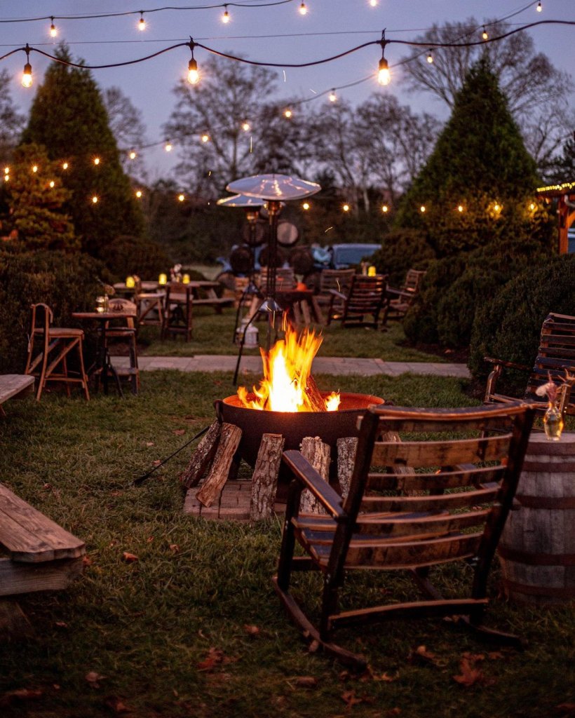 chairs gathered around fire pit at dusk with string lights above