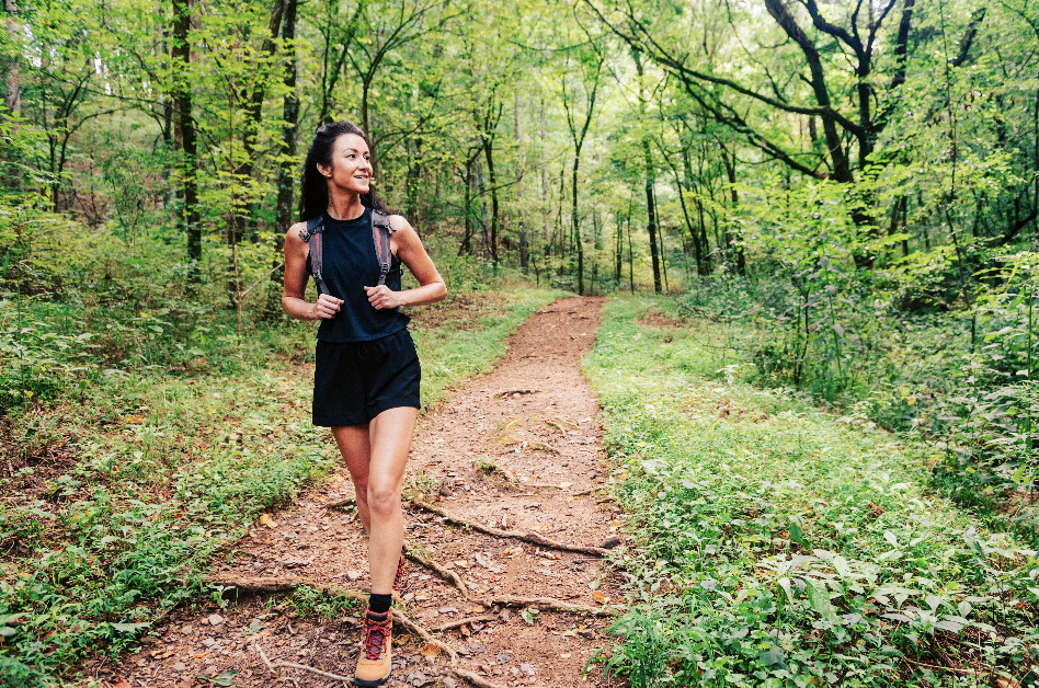 A woman in athletic wear smiles as she hikes a forest trail surrounded by lush greenery in Williamson County, Tennessee.