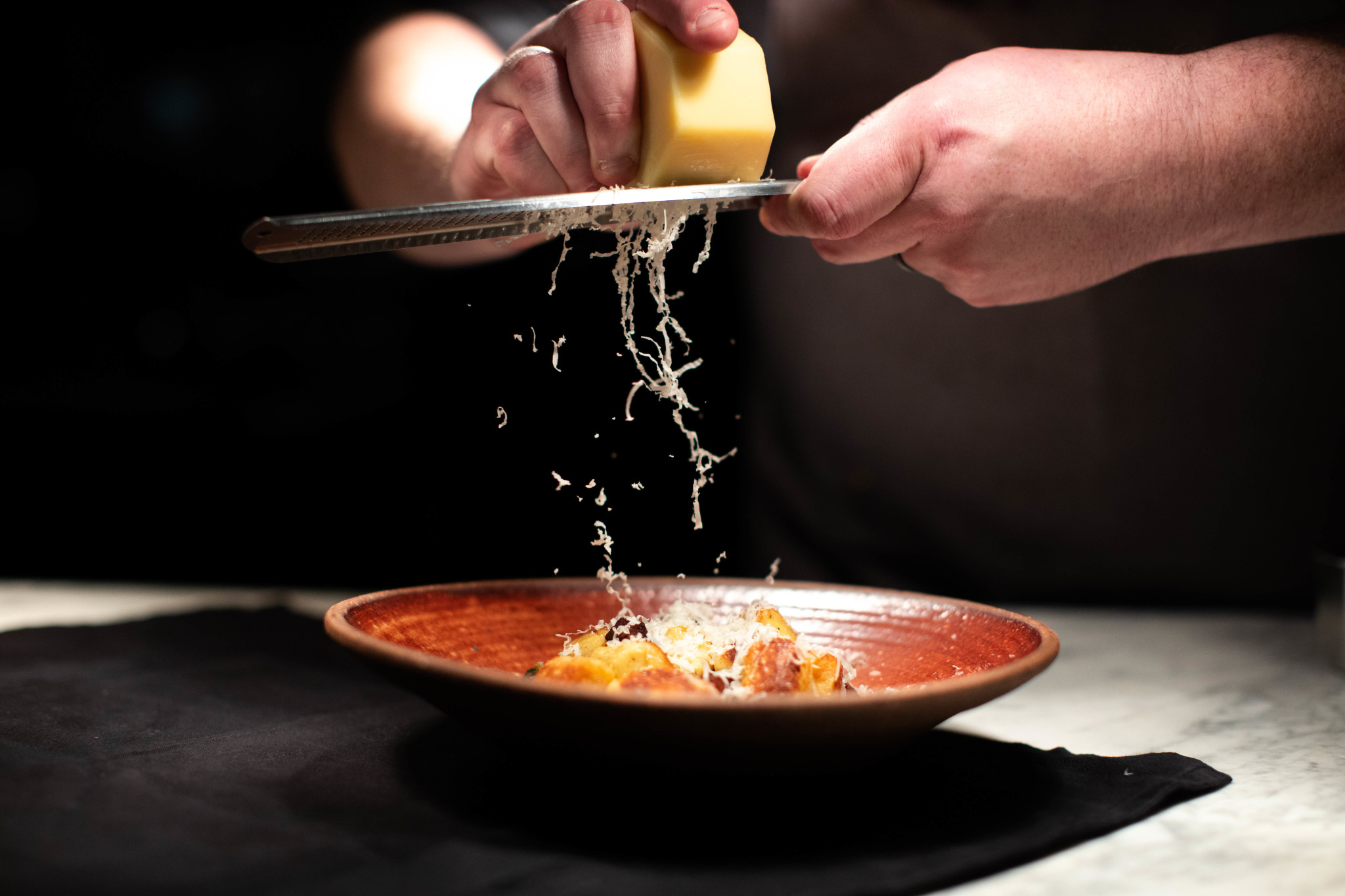 A chef's hands grate Parmesan cheese over a dish of pasta in a rustic bowl in Williamson County, Tennessee.
