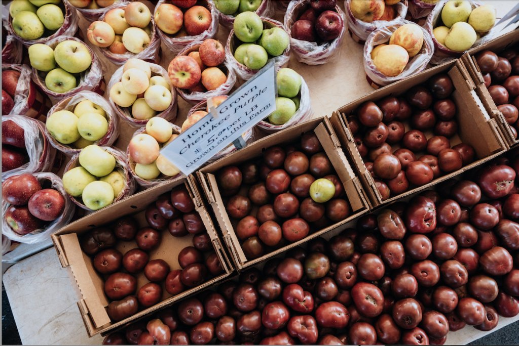 A variety of apples and tomatoes are displayed in cardboard boxes at a market in Williamson County, Tennessee.