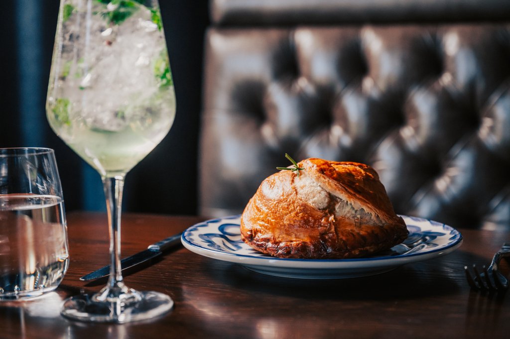 A golden-brown pastry sits on a blue-rimmed plate with a glass of sparkling water and mint nearby in Williamson County, Tennessee.