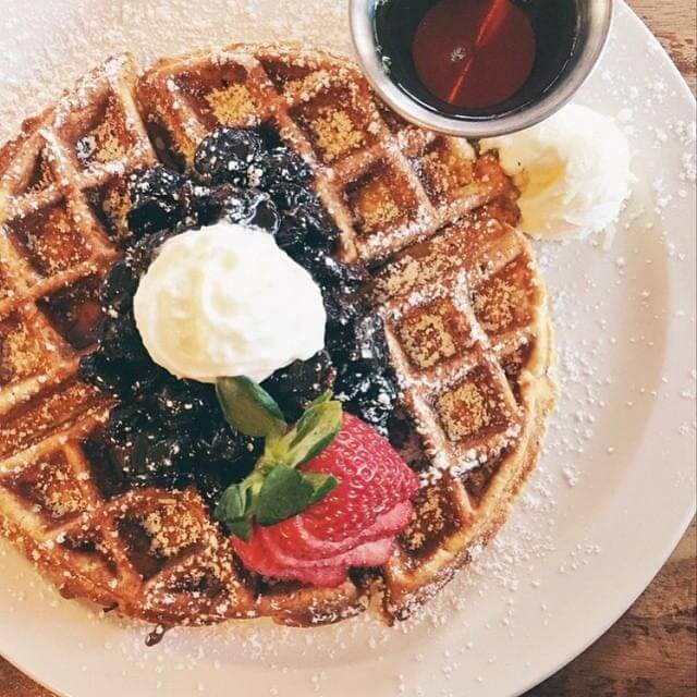 A delicious waffle topped with whipped cream, berries, and a strawberry, served with syrup in Williamson County, Tennessee.