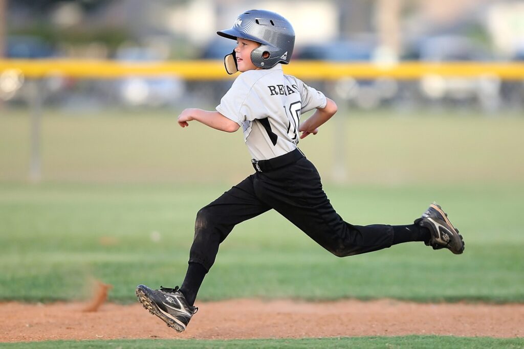 A young baseball player, wearing a helmet and uniform, sprints towards first base in Williamson County, Tennessee.