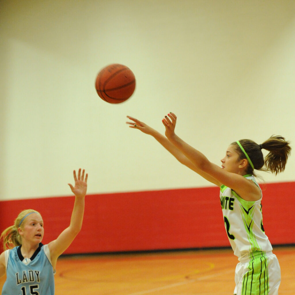 Two female basketball players, one in blue and one in green, are reaching for a basketball in mid-air in Williamson County, Tennessee.