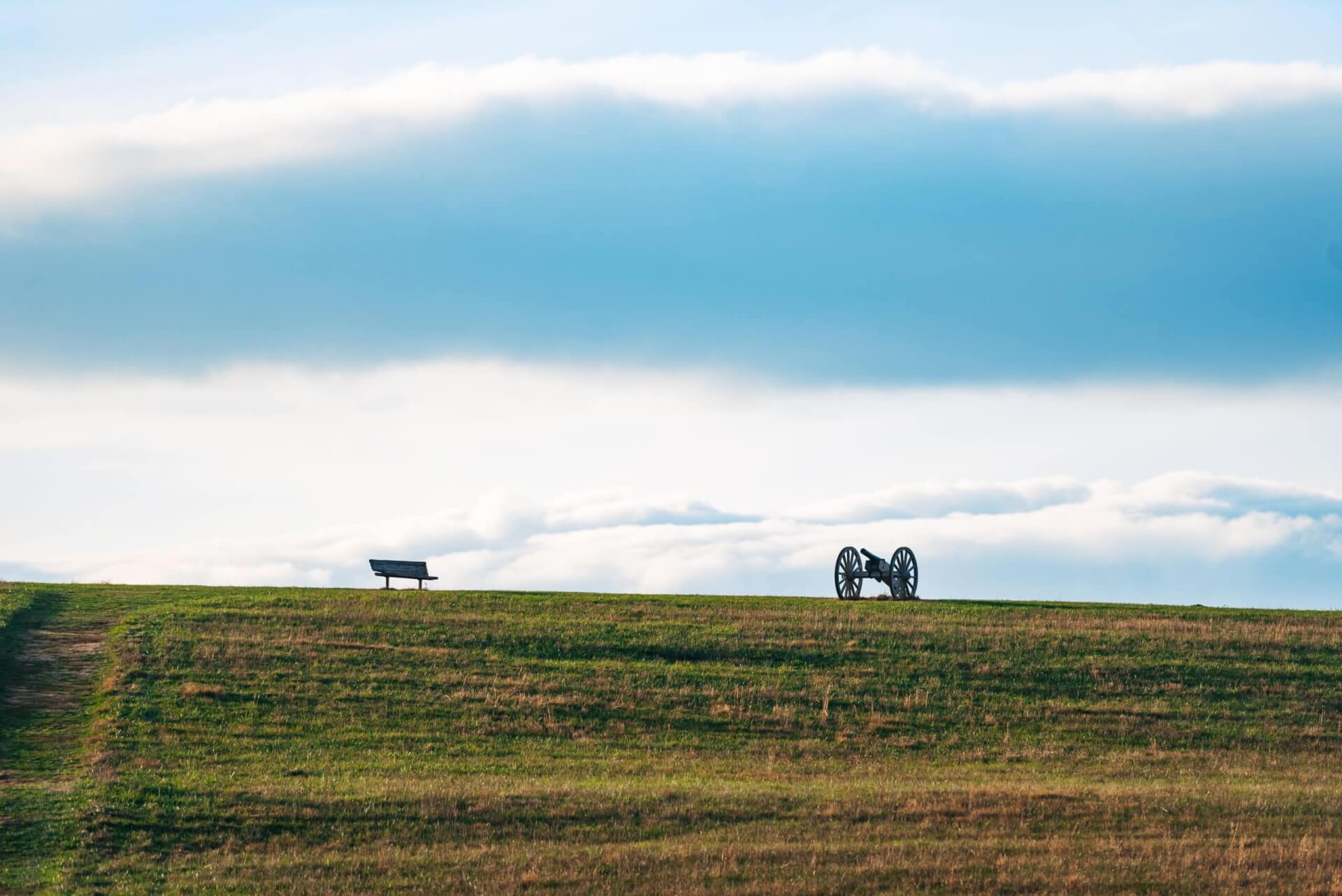 A lone bench overlooks a vast grassy field with a cannon in the distance in Williamson County, Tennessee.