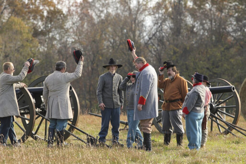 Historical reenactors in period costumes gather around a cannon in a grassy field in Williamson County, Tennessee.