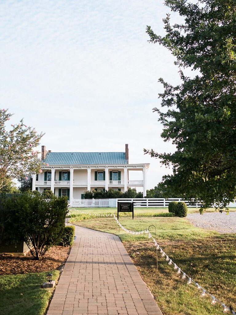 A brick pathway leads to a white two-story house with a porch and green shutters in Williamson County, Tennessee.