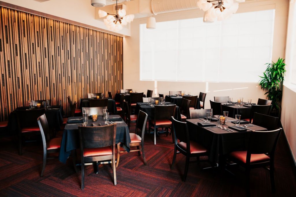 A modern restaurant dining room with black tables, red chairs, and a wooden accent wall in Williamson County, Tennessee.