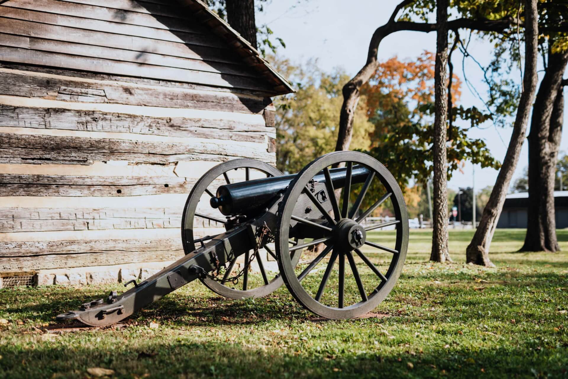 Battle of Franklin Trust An old cannon with large wheels rests on grass beside a rustic wooden cabin in Williamson County, Tennessee.