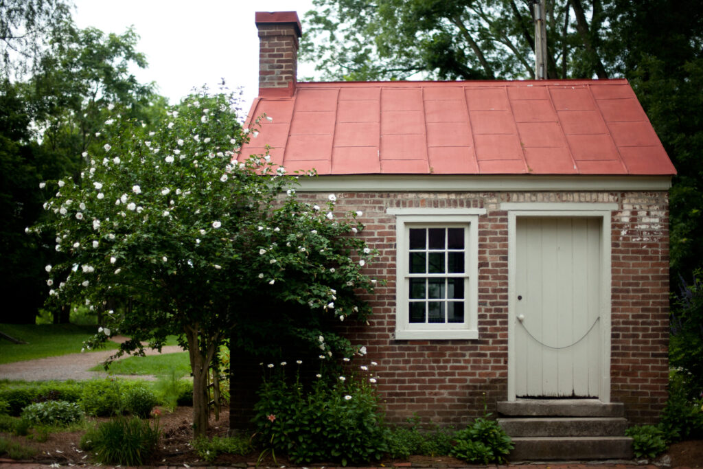 A quaint brick cottage with a red metal roof and white door nestled among lush greenery in Williamson County, Tennessee.