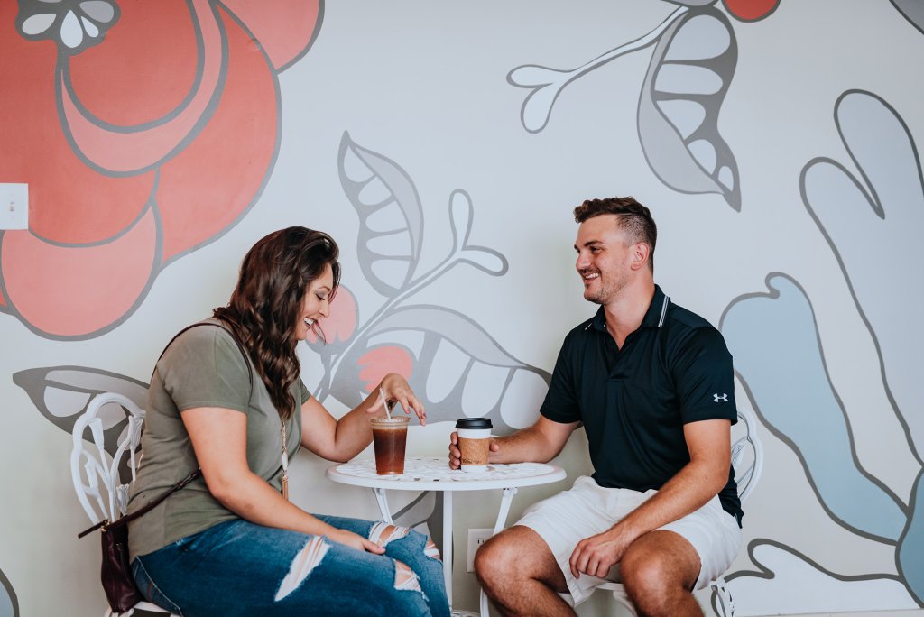 A couple enjoys iced coffee at a small table against a floral mural in Williamson County, Tennessee.