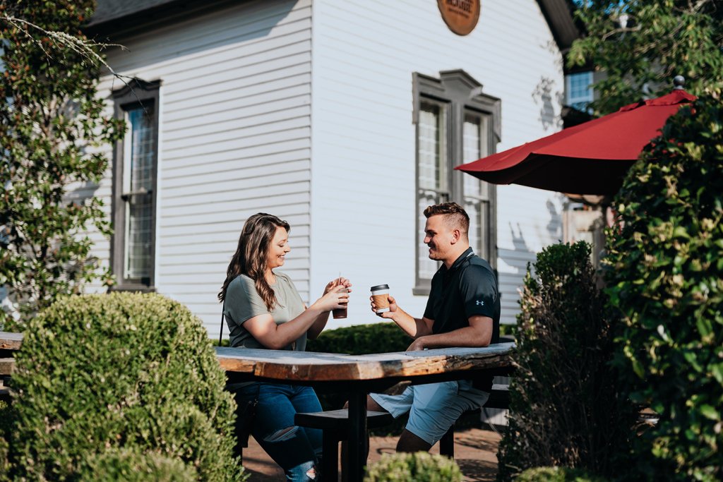 A couple enjoys coffee at an outdoor table under a red umbrella, surrounded by greenery in Williamson County, Tennessee.