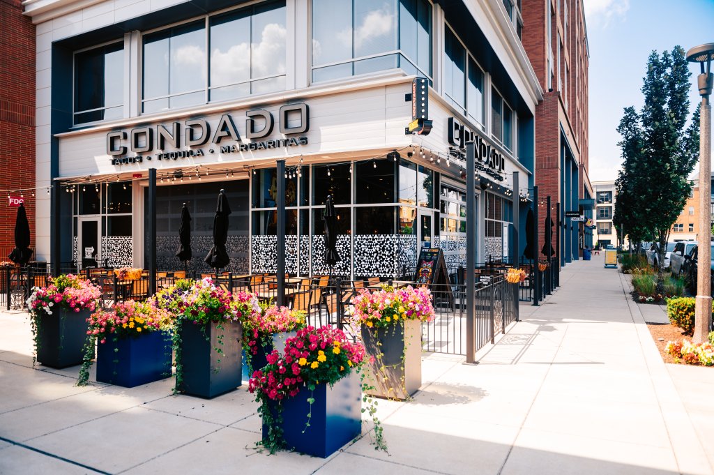 A vibrant outdoor seating area at Condado restaurant, adorned with colorful flower pots and black umbrellas, inviting patrons to enjoy tacos, tequila, and margaritas in Williamson County, Tennessee.