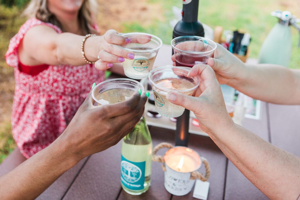 Four women cheerfully clink plastic cups filled with beverages at an outdoor table in Williamson County, Tennessee.