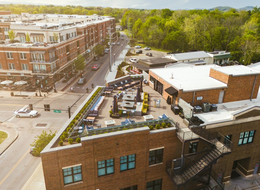 A bustling urban scene with a mix of modern and historic buildings, a rooftop garden, and a busy street filled with cars and pedestrians in Williamson County, Tennessee.