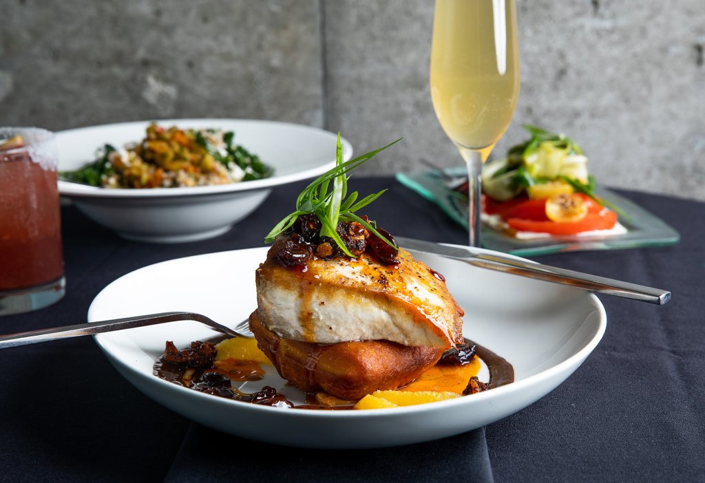 A gourmet dish featuring seared fish on a sweet potato cake with orange slices and a glass of sparkling wine in Williamson County, Tennessee.