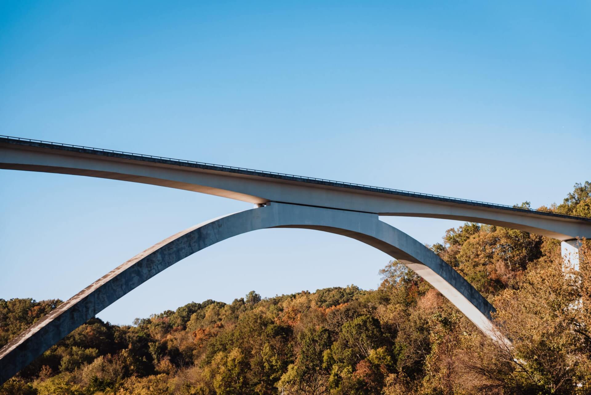 A modern concrete bridge with a distinctive curved arch spans a valley, set against a backdrop of colorful autumn trees in Williamson County, Tennessee.