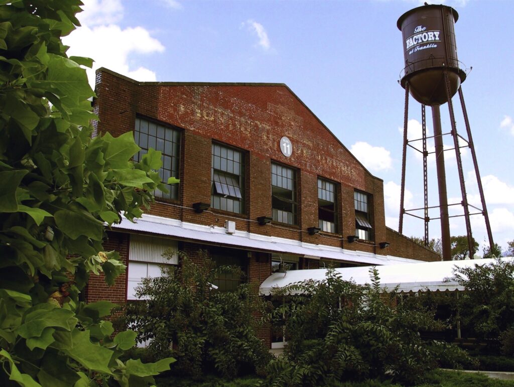 A red brick warehouse with a water tower and lush greenery in the foreground in Williamson County, Tennessee.