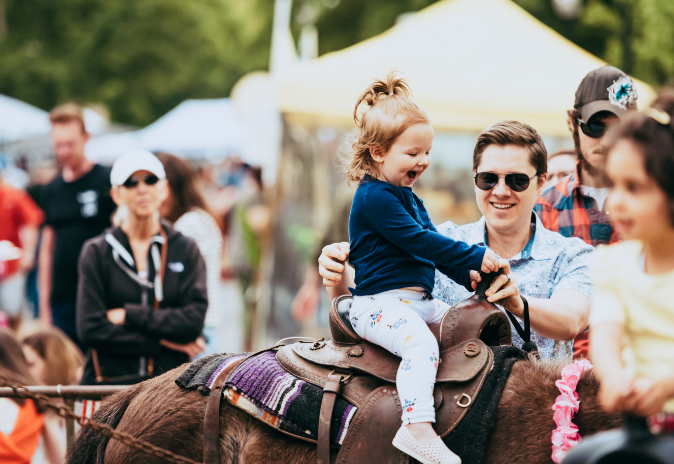 A young girl joyfully rides a pony at a fair, accompanied by her smiling father in Williamson County, Tennessee.