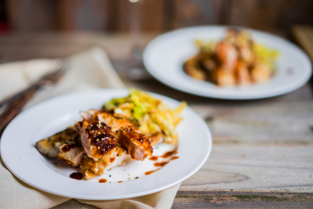 Two plates of food with crispy chicken, vegetables, and sauce on a wooden table in Williamson County, Tennessee.