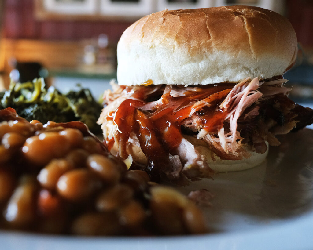 A pulled pork sandwich with barbecue sauce on a bun, served with baked beans and collard greens in Williamson County, Tennessee.