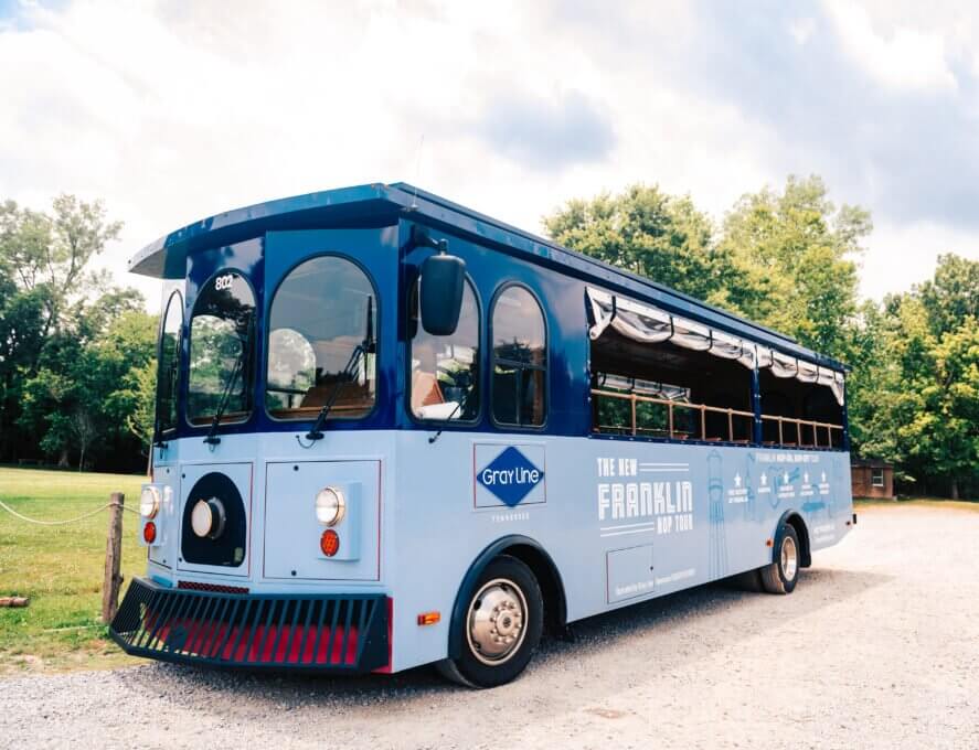 A vintage-style blue trolley bus with open sides and red accents parked on gravel in Williamson County, Tennessee.