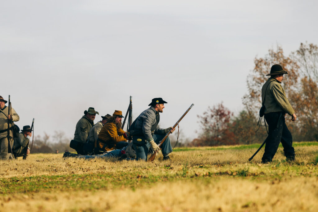 Civil War reenactors in period uniforms march across a grassy field with rifles in Williamson County, Tennessee.