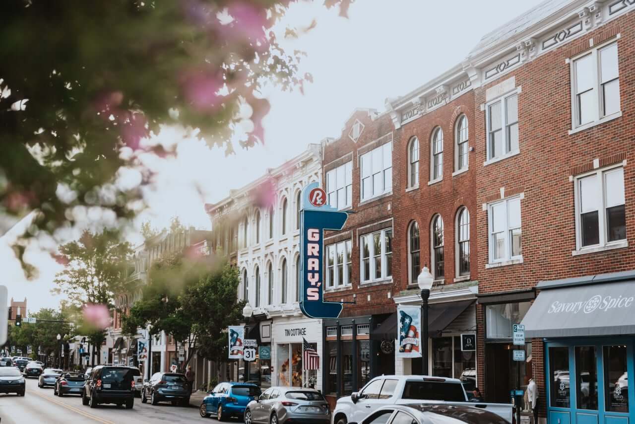 A bustling downtown street with historic brick buildings, cars, and a prominent neon sign in Williamson County, Tennessee.