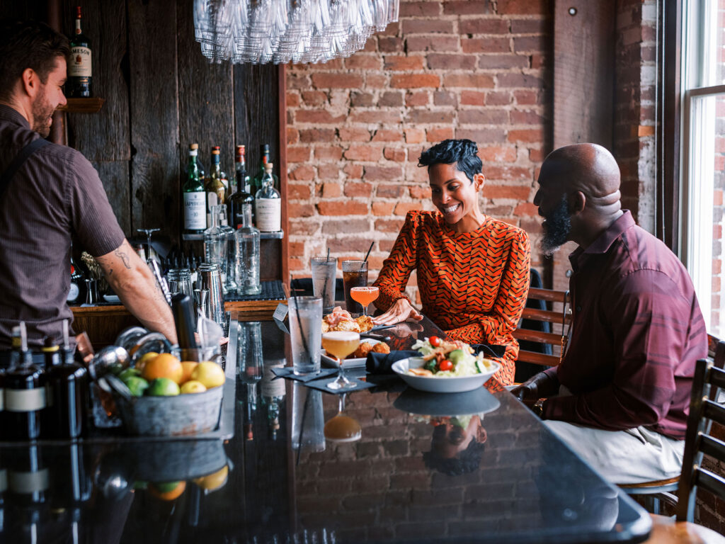 Three people enjoy a meal at a brick-walled restaurant bar with a variety of drinks and food in Williamson County, Tennessee.