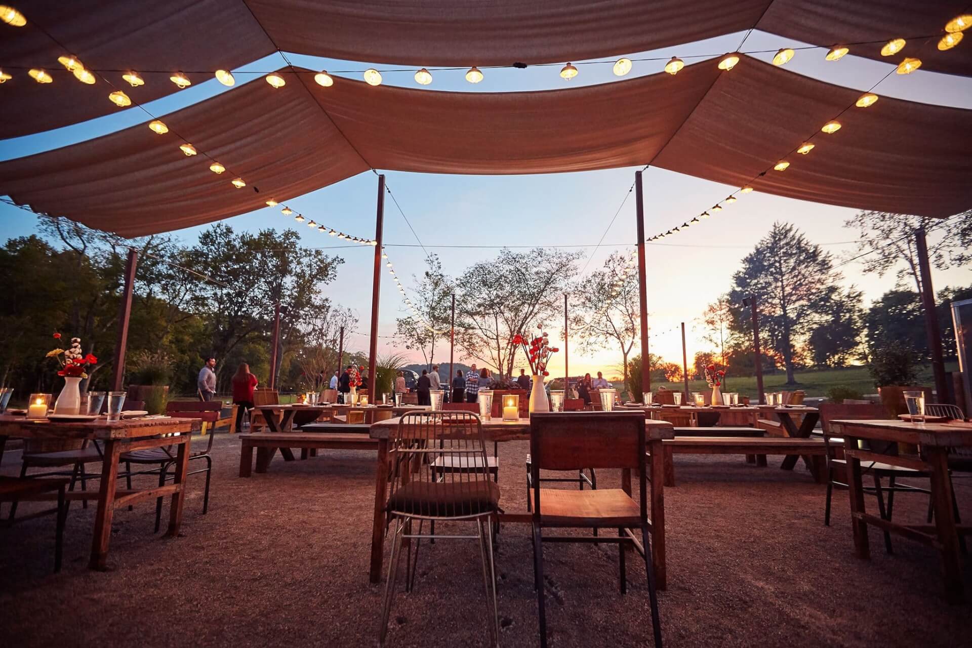 Outdoor dining area with wooden tables and chairs under a large tent illuminated by string lights in Williamson County, Tennessee.
