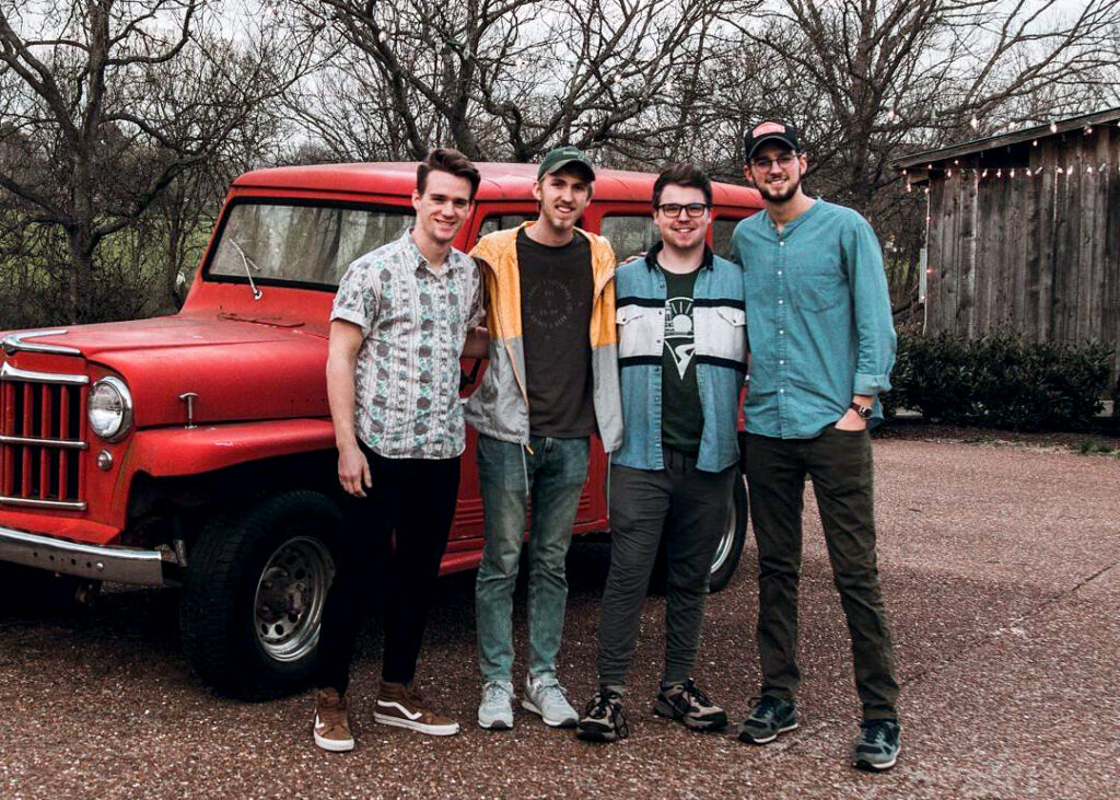 Four young men stand together smiling in front of a vintage red Jeep Wrangler in Williamson County, Tennessee.