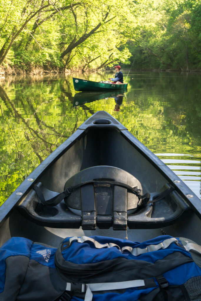 A serene river scene with a canoeist paddling towards a lone kayaker amidst lush greenery in Williamson County, Tennessee.