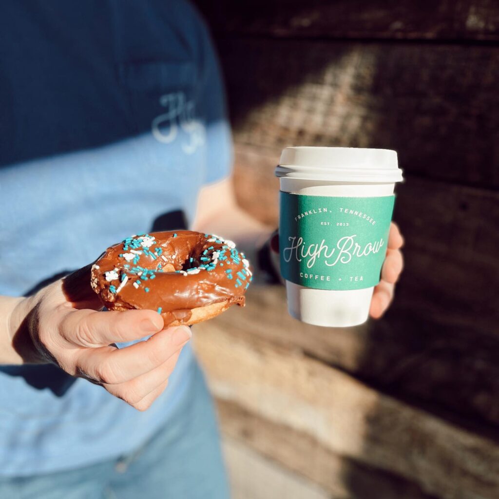 A person holds a chocolate donut with blue sprinkles and a green coffee cup with a white lid in Williamson County, Tennessee.