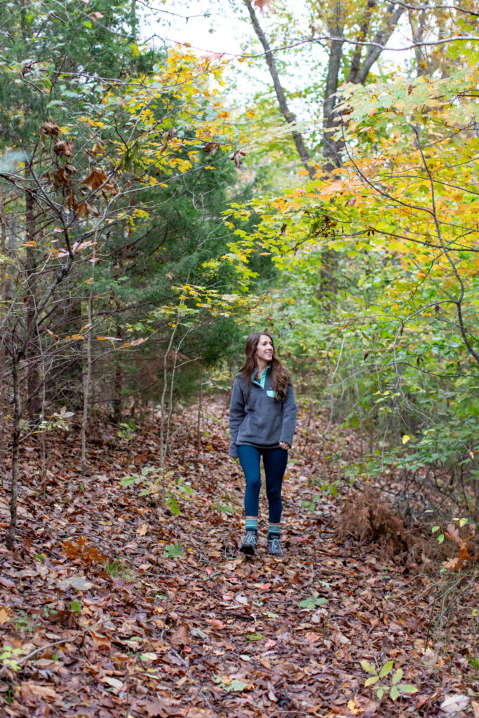 A woman in a gray hoodie walks through a colorful autumn forest with fallen leaves in Williamson County, Tennessee.
