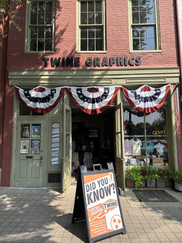 A brick storefront with patriotic bunting and a sign reading 'Twine Graphics' above the entrance in Williamson County, Tennessee.
