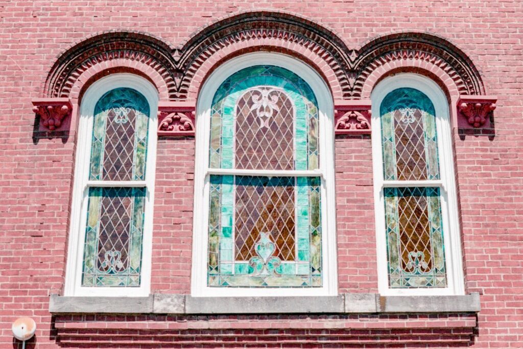 Three ornate stained glass windows with intricate designs set in a red brick wall in Williamson County, Tennessee.