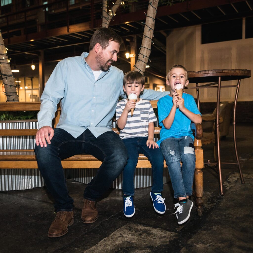 A man and two boys enjoy ice cream on a bench in a dimly lit outdoor area in Williamson County, Tennessee.