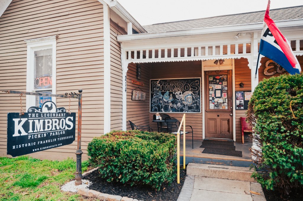 A quaint, historic building with a welcoming porch, featuring a sign for 'The Legendary Kimbros Pickin' Parlor' and a vibrant chalkboard menu in Williamson County, Tennessee.
