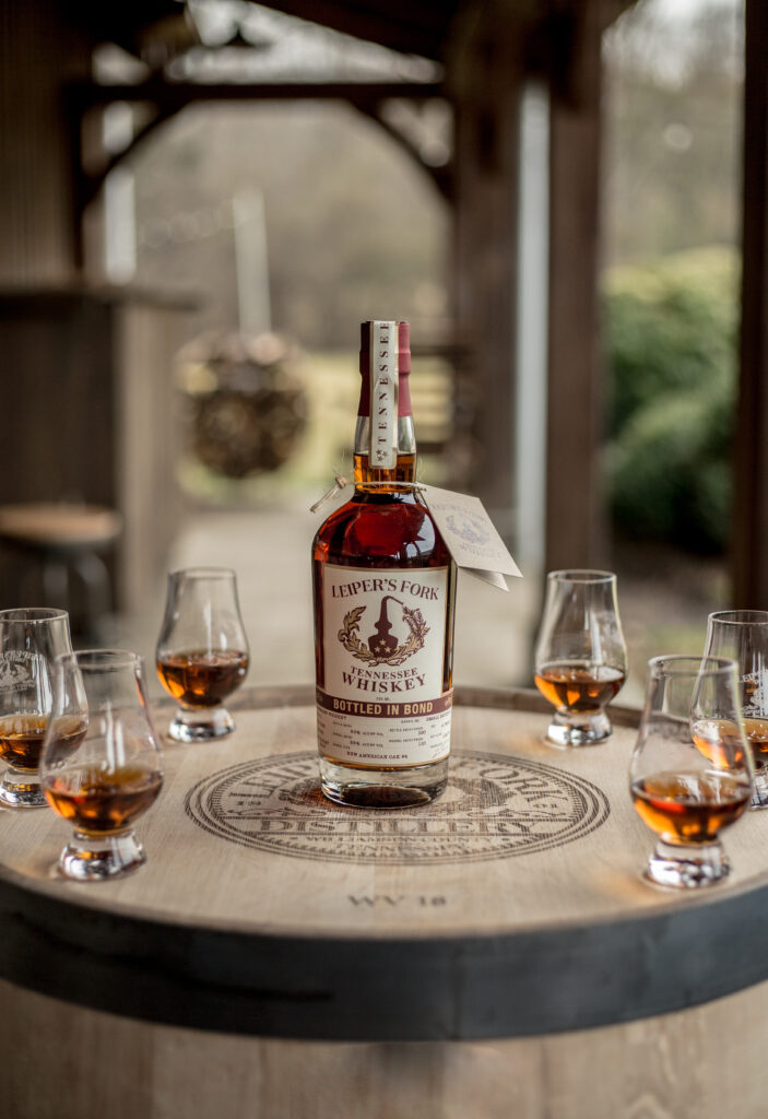 A bottle of Leiper's Fork Tennessee Whiskey sits on a wooden barrel surrounded by tasting glasses in Williamson County, Tennessee.