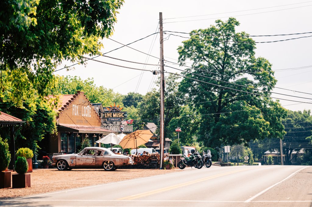 A vintage car and motorcycles parked outside a rustic music venue with outdoor seating and live music signage in Williamson County, Tennessee.