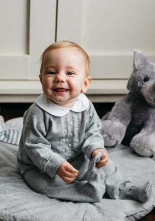 A cheerful baby boy sits on a soft mat, surrounded by plush toys, wearing a cozy gray outfit in Williamson County, Tennessee.