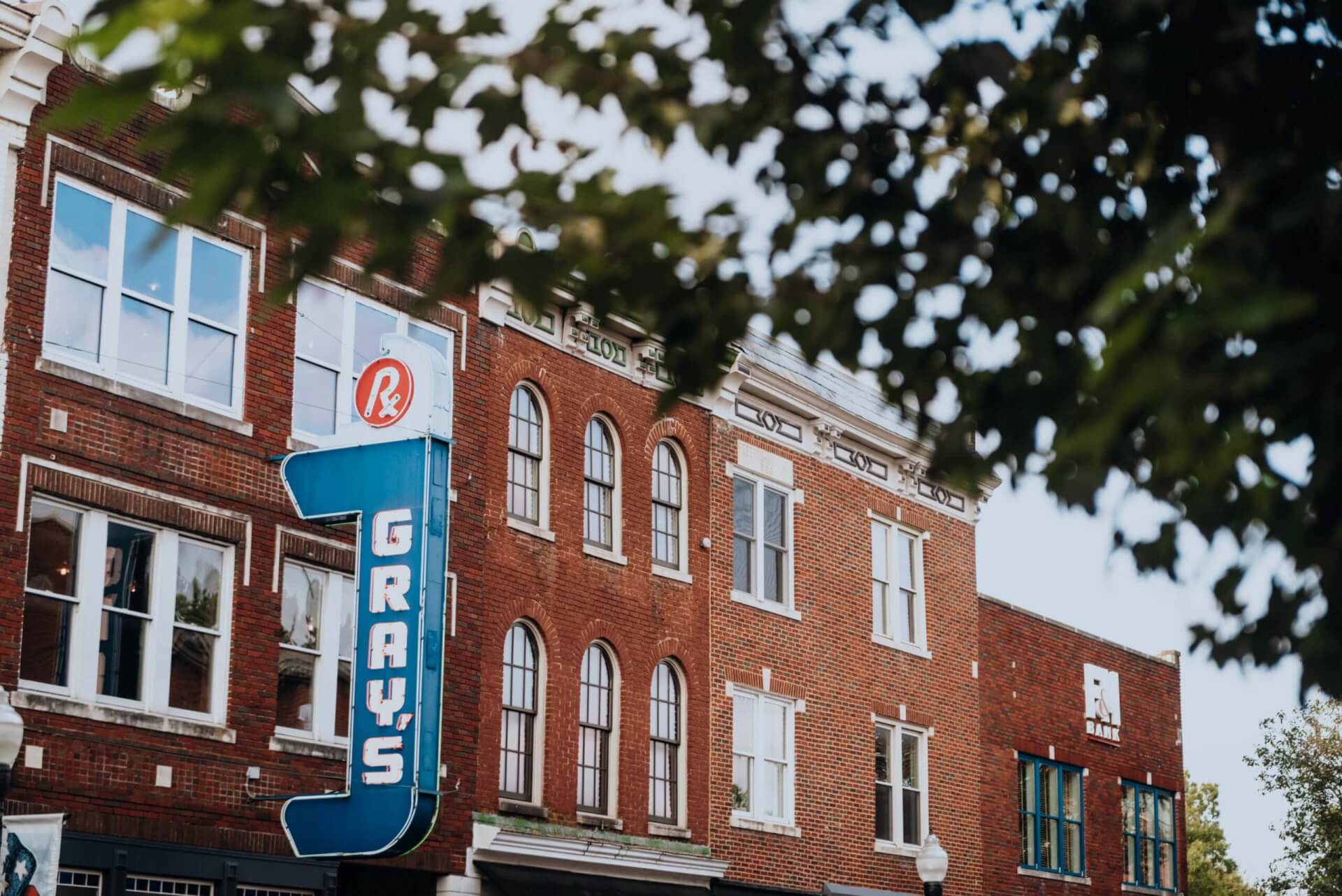 A row of red brick buildings with arched windows and a blue neon sign reading 'Gray's' on one of them in Williamson County, Tennessee.