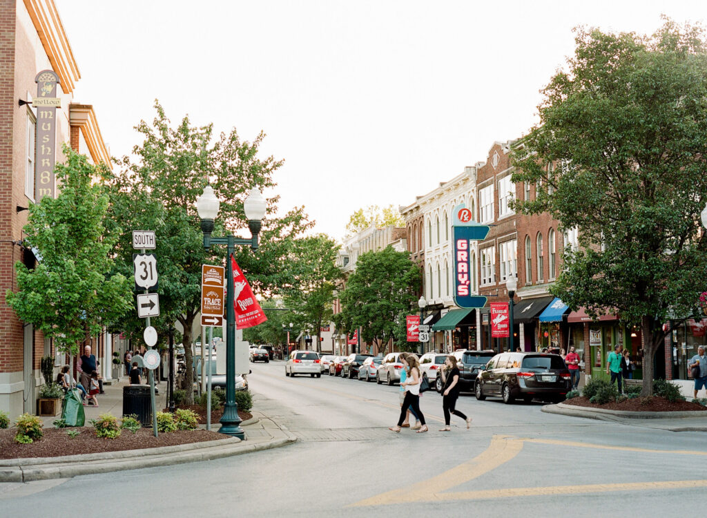 A bustling downtown street scene with pedestrians, cars, and colorful storefronts in Williamson County, Tennessee.